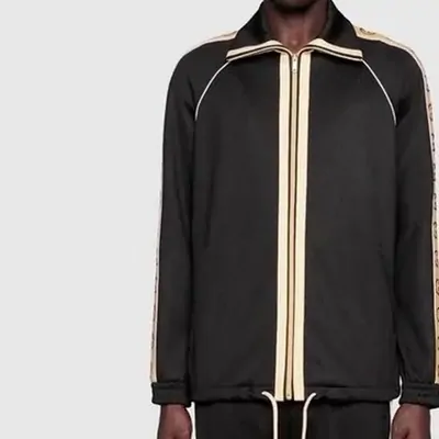 A black zip-up track jacket with cream side stripes shown on a mannequin