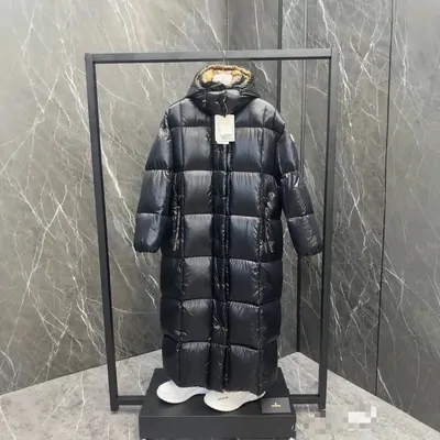 A long black quilted coat displayed on a stand against a marble wall